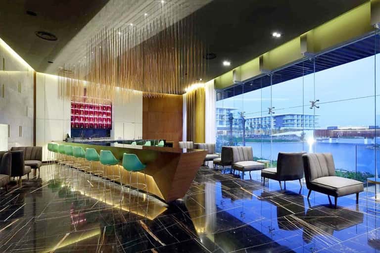 Upscale hotel bar and lounge with floor-to-ceiling windows, modern lighting, and waterfront views
