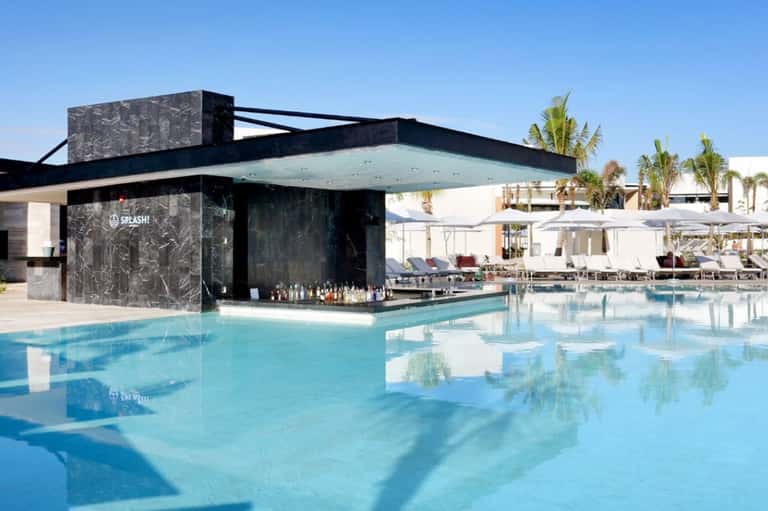 Modern black pool bar with glass overhang beside resort swimming pool and palm trees