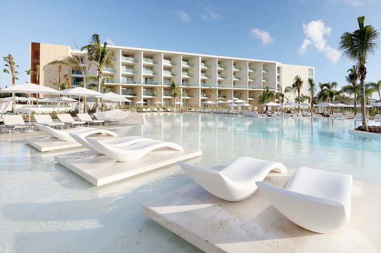 Modern beachfront resort pool with white lounge chairs, umbrellas, and ocean backdrop