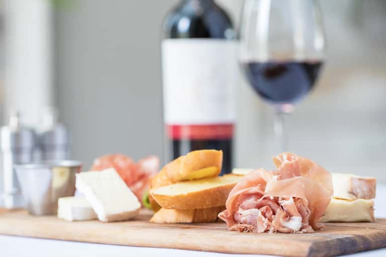 Charcuterie board with cured meats, cheese, and bread beside red wine glass