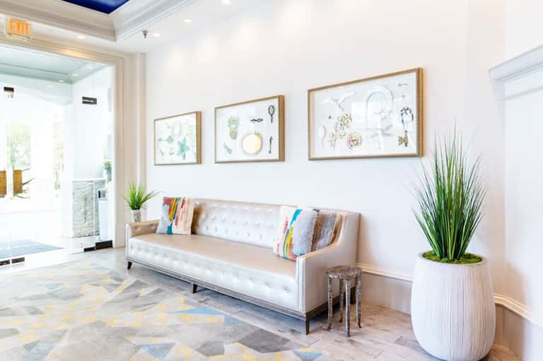 Modern hotel lobby with cream sofa, framed coastal artwork, potted plant, and bright natural lighting