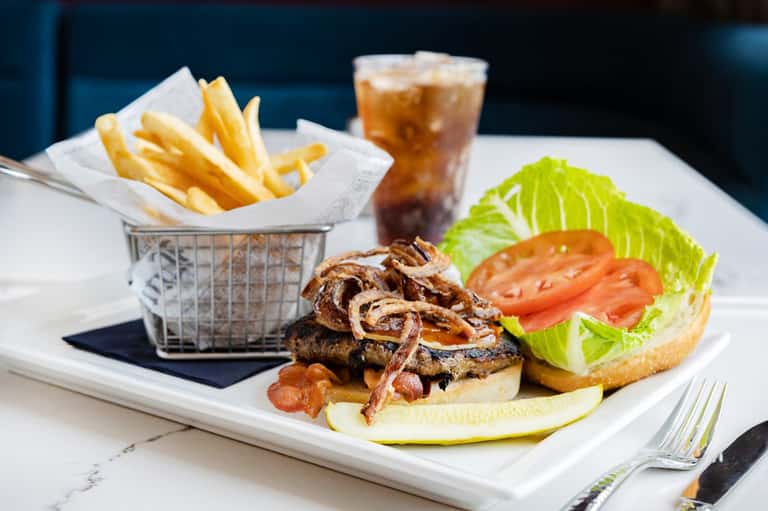 Gourmet burger with fries and beverage on white plate at resort restaurant