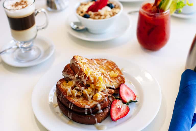 Gourmet breakfast plate with French toast, berries, coffee, and fresh juice on white table