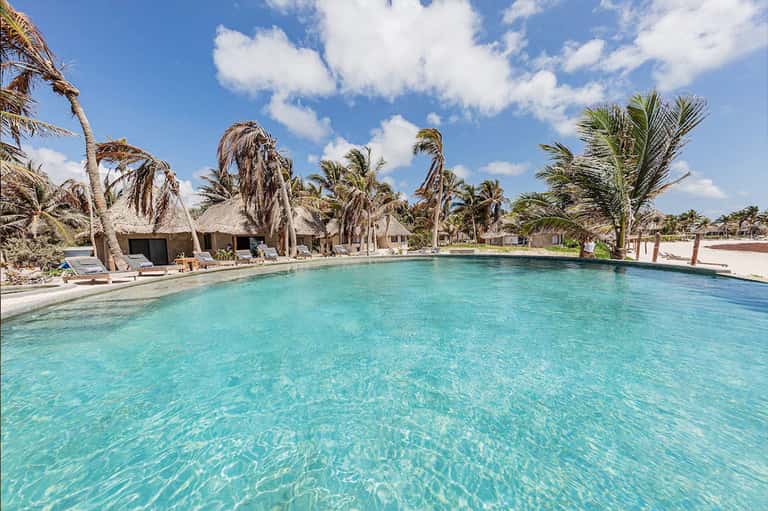 Lagoon-style pool with thatched-roof bungalows and palm trees on tropical beach