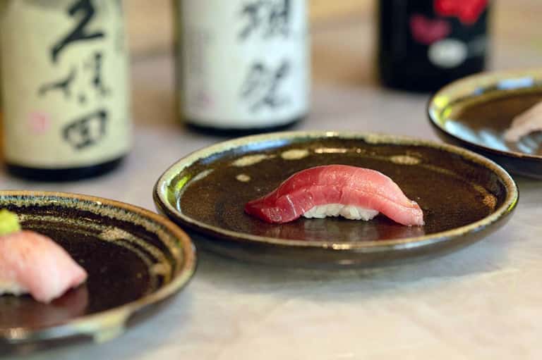 Sushi nigiri on dark ceramic plates with sake bottles in background