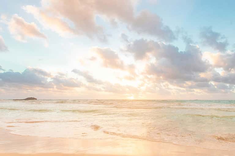 Serene beach at sunrise with calm waves, sandy shore, and soft clouds over ocean