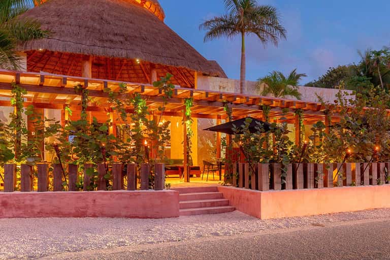 Illuminated beachfront restaurant with thatched roof and wooden pergola at dusk