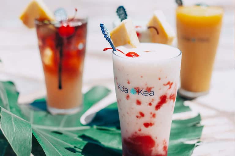 Colorful tropical cocktails with fruit garnishes on green leaf napkins at a beach bar