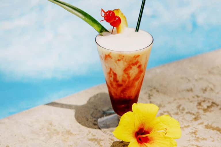 Tropical cocktail with fruit garnish and pink umbrella by swimming pool