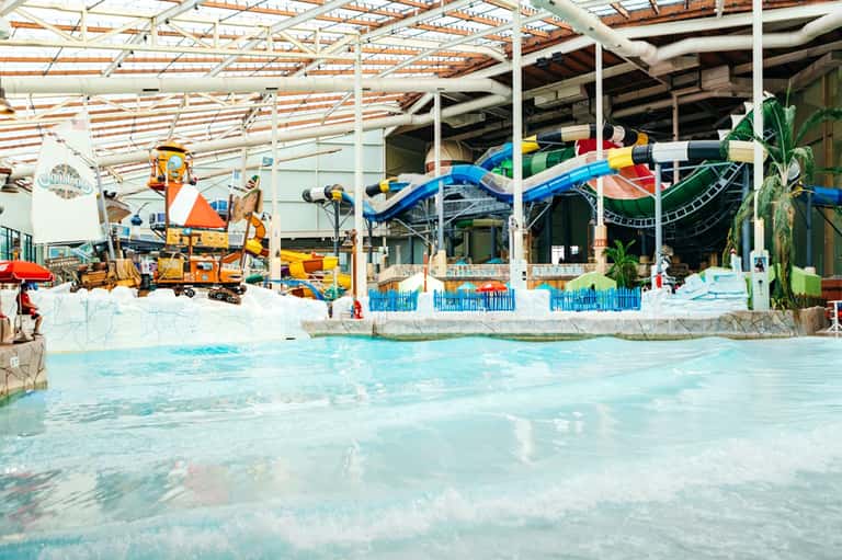 Indoor water park with retractable roof, colorful waterslides, shallow pools, and tropical themed entertainment area
