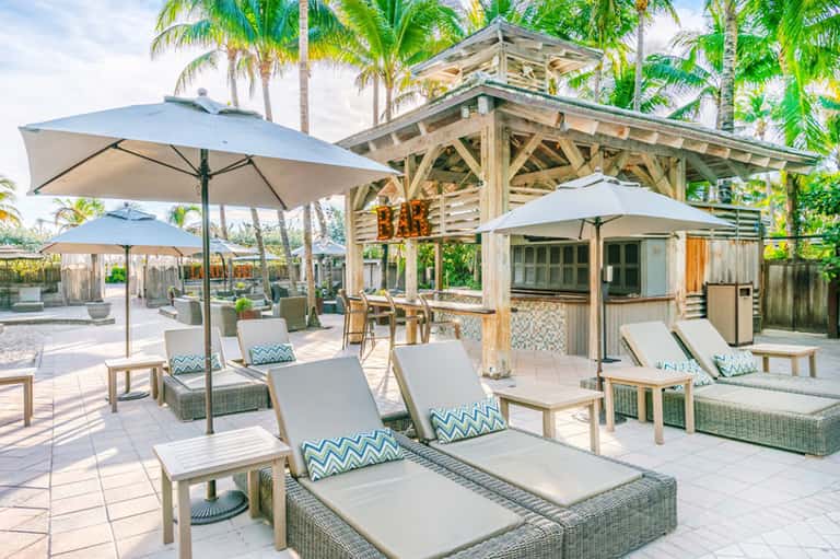 Beachfront bar and lounge area with umbrellas, loungers, and palm trees