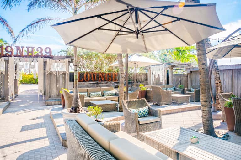 Upscale poolside lounge with large umbrellas, woven furniture, cushioned seating, and tropical landscaping