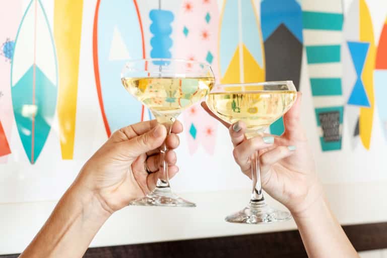 Two hands toasting with champagne glasses against colorful geometric party backdrop