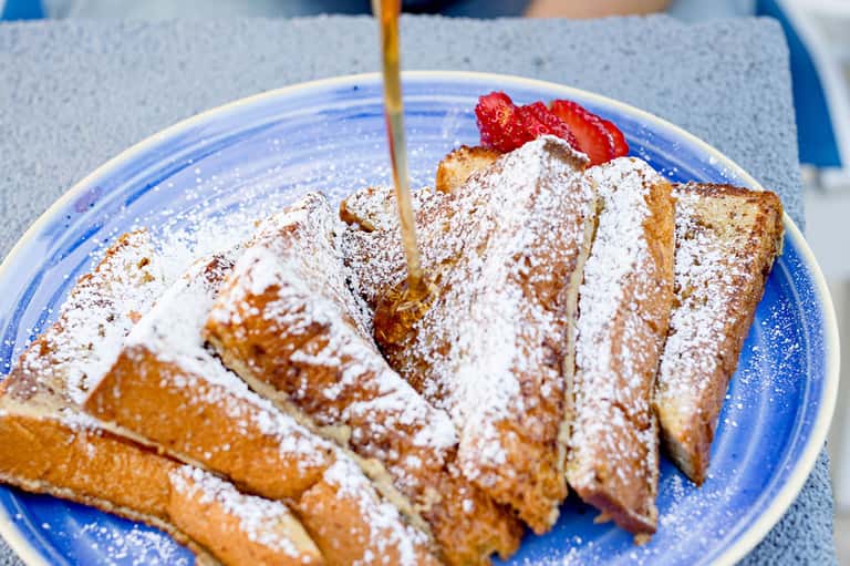 Powdered French toast slices with strawberries on blue plate with syrup being poured