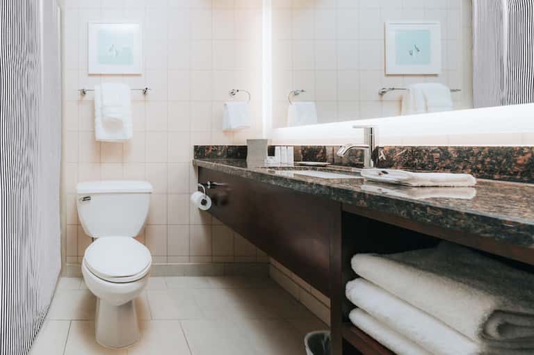 Clean hotel bathroom with white tile, double sink vanity, toilet, and white towels