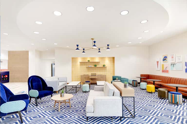 Contemporary lobby lounge with patterned rug, blue velvet chair, cream sofas, and modern pendant light