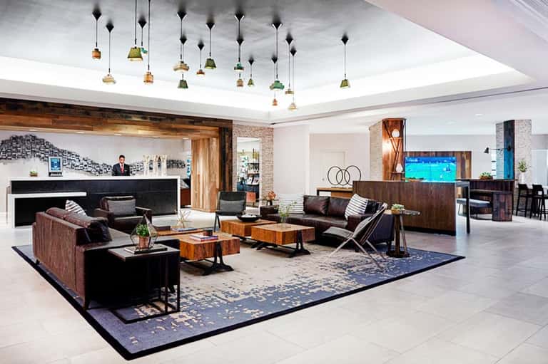 Contemporary hotel lobby with modern furnishings, pendant lights, fireplace, and dark wood accents