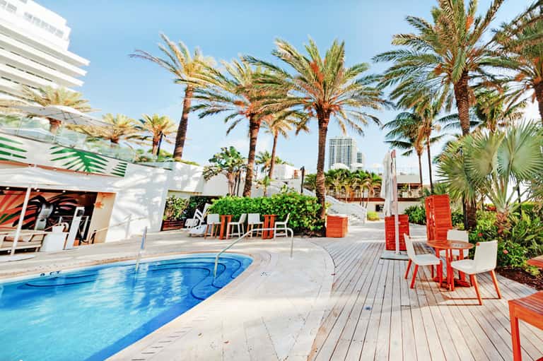 Resort deck with small pool, palm trees, red chairs, and modern white architecture