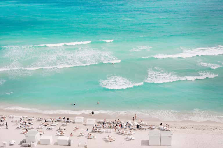 Overhead view of crowded beach with turquoise ocean waves and white beach cabanas