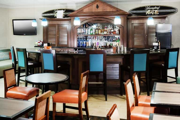 Hotel bar interior with wooden back bar, turquoise bar stools, and orange leather dining chairs