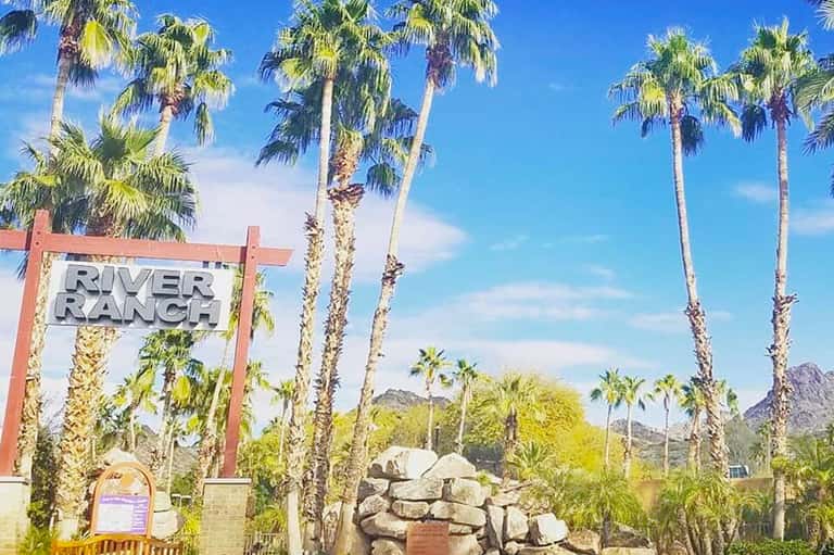 River Ranch sign with tall palm trees and desert mountains in background