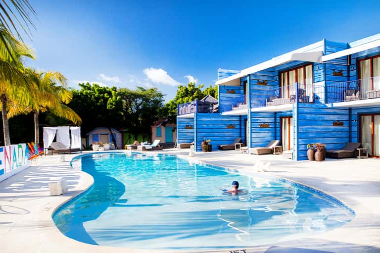 Bright blue pool with modern cabanas and palm trees under clear blue sky