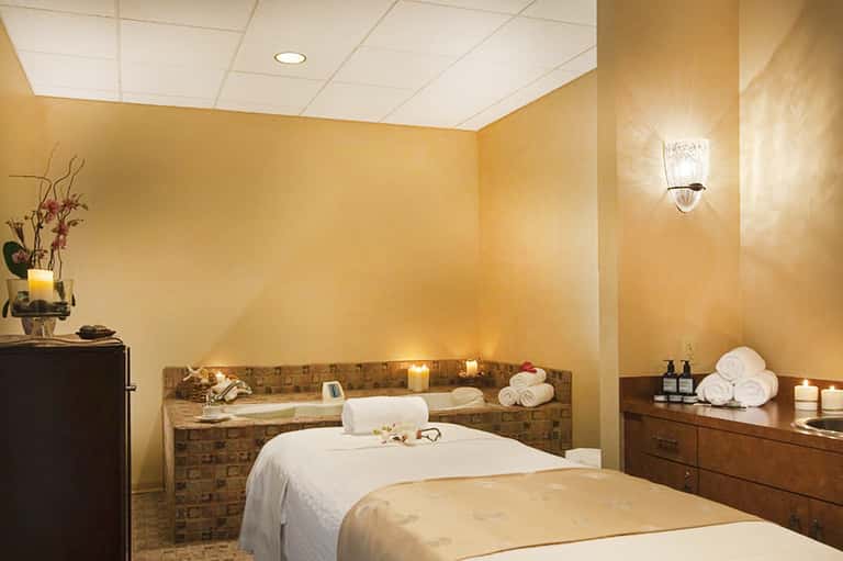Spa treatment room with massage tables, warm lighting, and towel storage