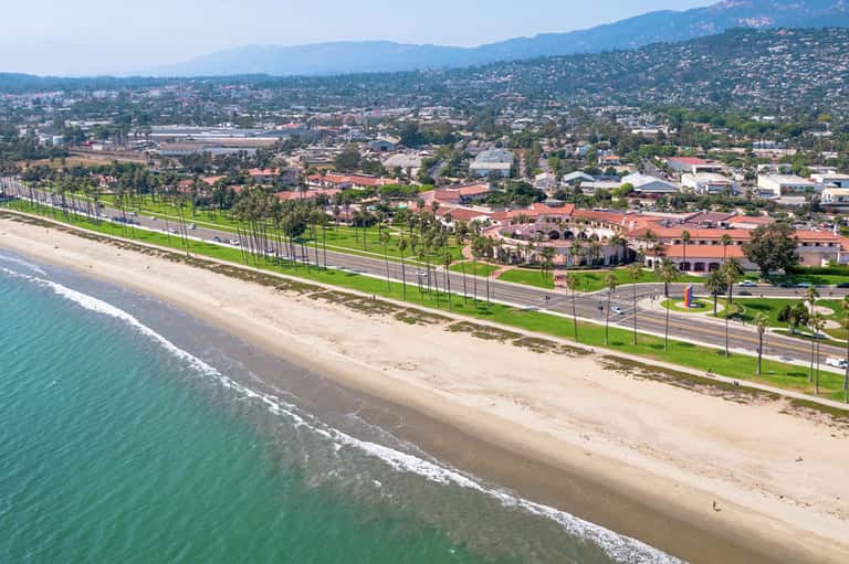 Coastal beachfront area with sand, grass, and residential buildings