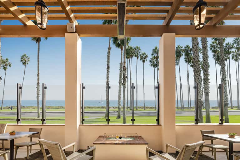 Oceanfront pergola dining area with palm trees, glass railings, and ocean horizon view