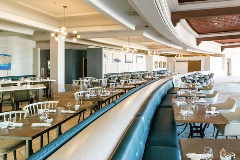 Upscale restaurant dining room with long tables, modern lighting, and elegant place settings