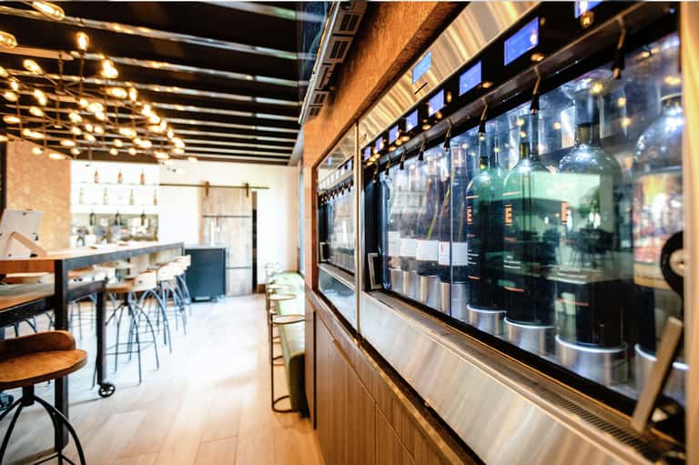 Modern beverage bar with illuminated shelving, glass display cases, and contemporary counter seating