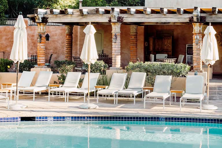 Pool area with lounge chairs, white umbrellas, and rustic brick building with classical columns