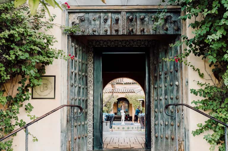 Ornate green doorway framed by ivy leading to courtyard with arches