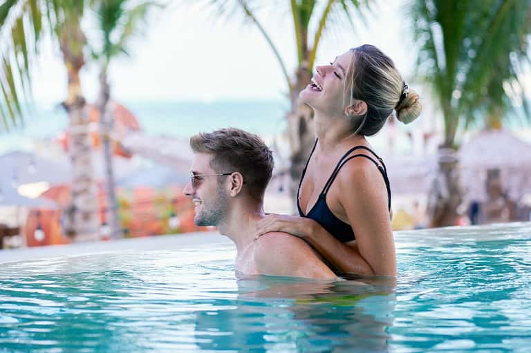 Couple relaxing in resort infinity pool with palm trees and ocean view at tropical beach