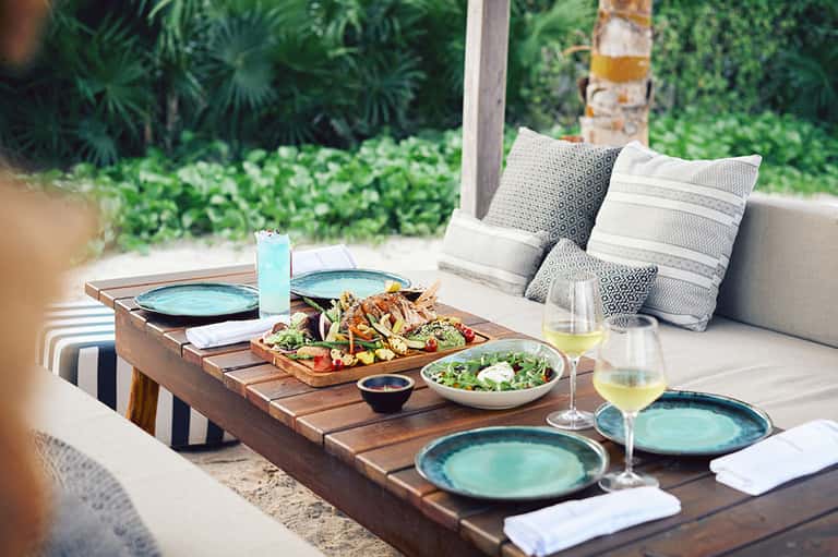 Outdoor dining setup with grilled seafood, salads, and wine glasses on wooden table