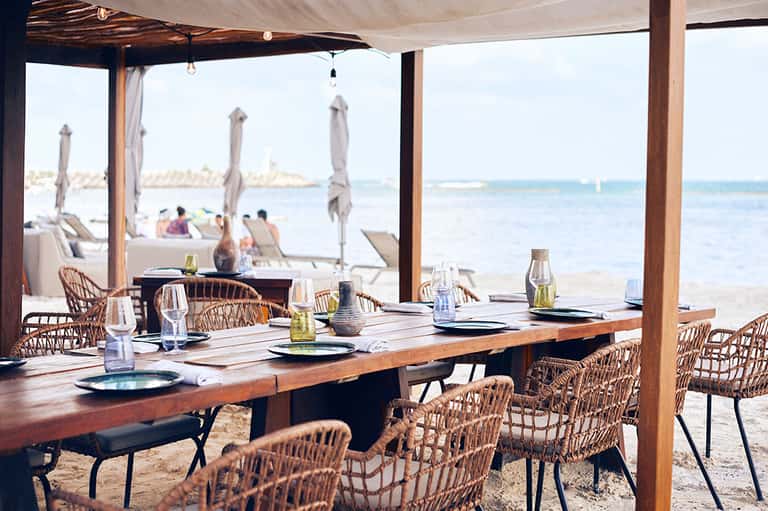 Beachfront dining pavilion with wooden table, wicker chairs, and ocean views