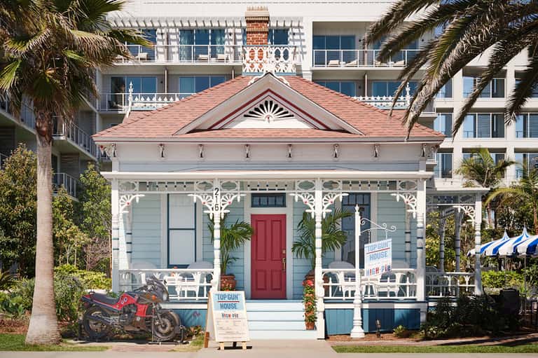 Historic Victorian cottage with blue-gray siding, red door, white trim, and modern hotel building behind