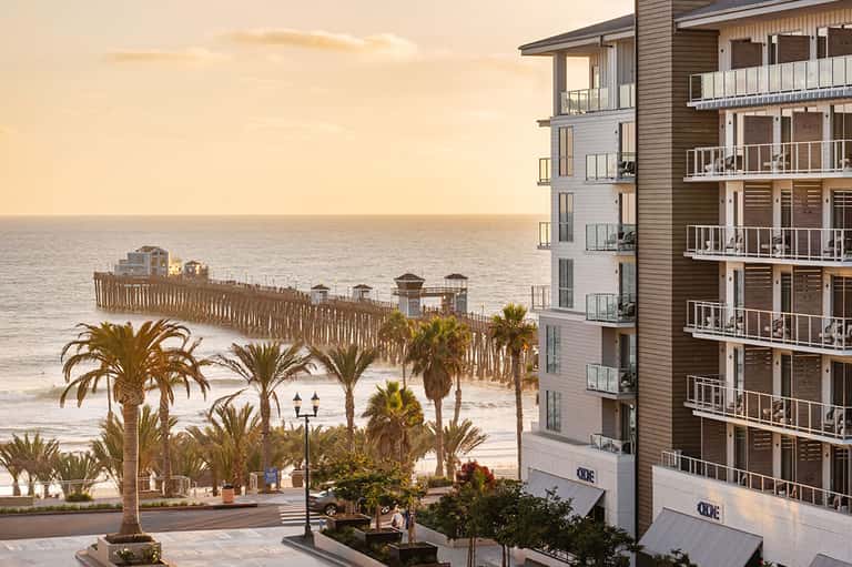 Oceanfront resort building at golden hour with palm trees and wooden boardwalk leading to sandy beach