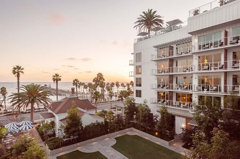 Beachfront resort at dusk with palm trees, multi-story white building, and coastal views