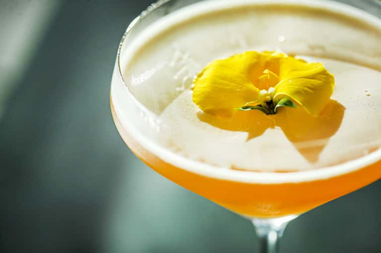 Cocktail with yellow flower garnish in coupe glass with orange liqueur base
