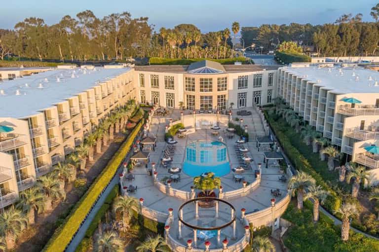 Aerial view of resort with multiple pools, courtyard, surrounding residential buildings and waterfront landscape