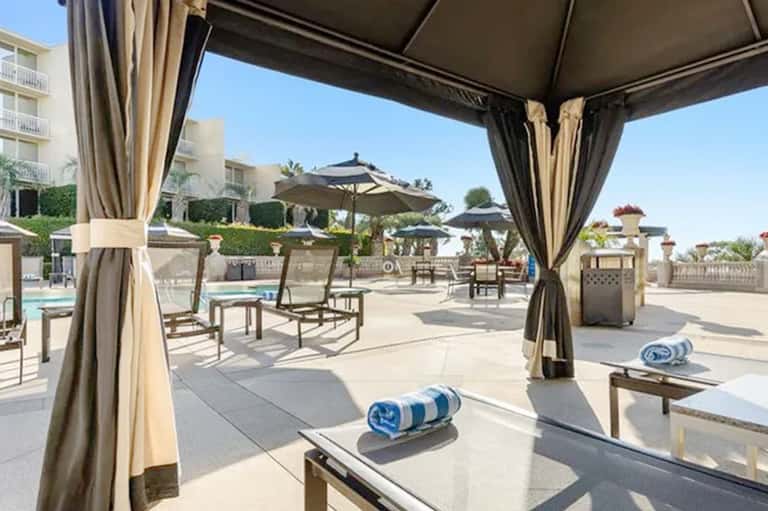 Covered outdoor seating pavilion with curtains overlooking resort pool and landscaping
