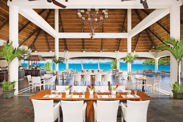 Beachfront dining pavilion with wooden ceiling, ocean view, and white table settings