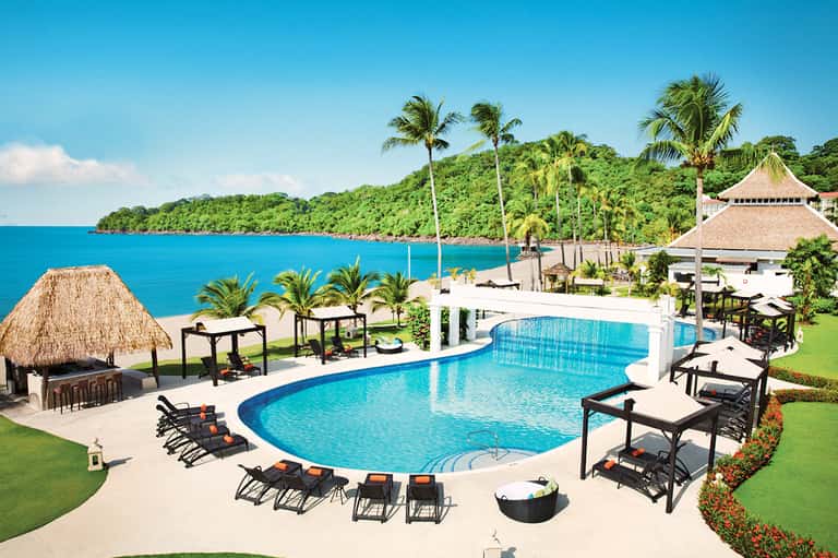 Luxury resort pool overlooking tropical ocean with palm trees and beach cabanas