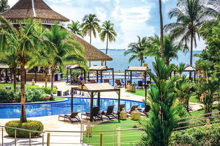 Beachfront resort with multiple pools, thatched umbrellas, palm trees, and ocean view