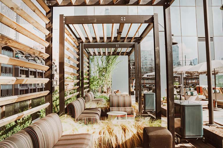 Modern rooftop lounge with wooden pergolas, striped chairs, city skyline views, and contemporary design