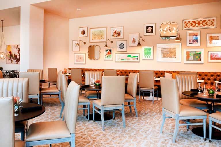 Modern restaurant dining room with peach walls, gallery wall art, and cream upholstered chairs