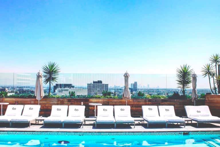 Luxury rooftop pool with white loungers and city skyline views under clear blue sky