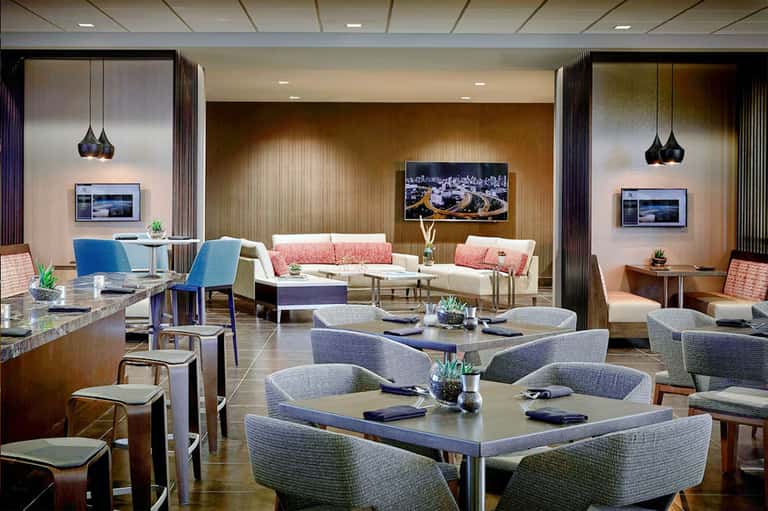 Upscale hotel lounge with modern furniture, coral accents, pendant lighting, and flat-screen TVs