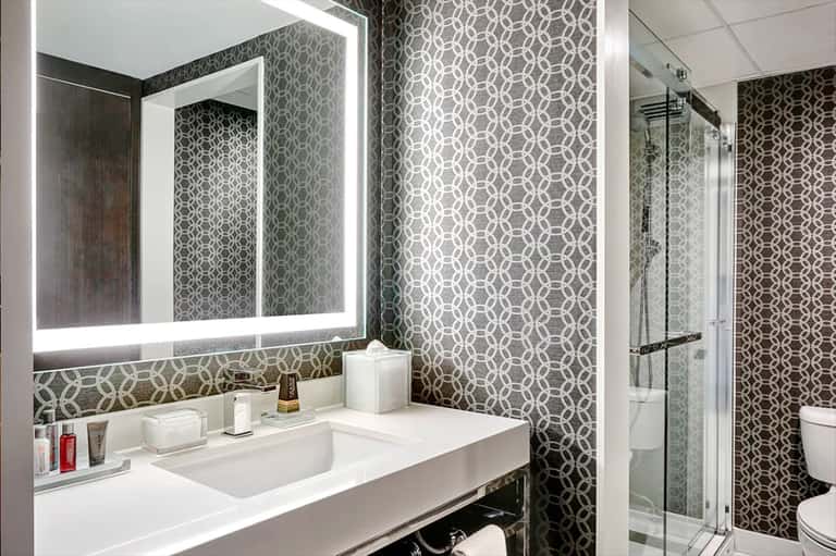 Modern bathroom with geometric patterned wallpaper, illuminated mirror, and glass shower